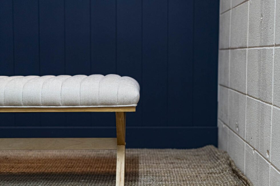 Landscape shot showcasing beach house photography set. natural fiber rug with white bench on a deep blue wood slat wall backdrop. neutral concrete wall to the right
