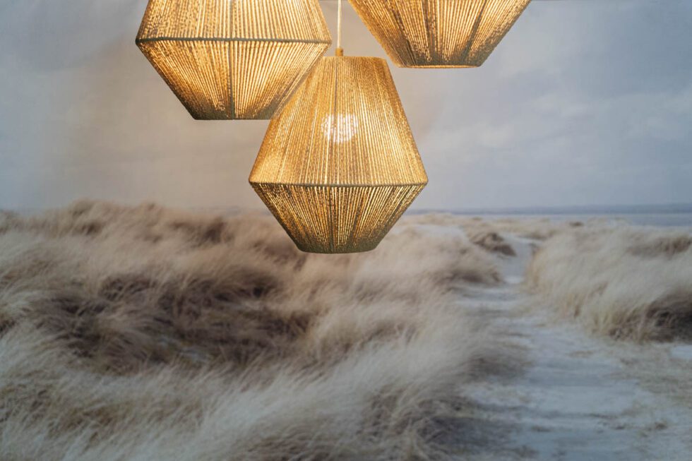 Landscape shot showcasing beach house photography set. Lit natural fiber chandelier (set of 3) with sandy beach framed photo in background