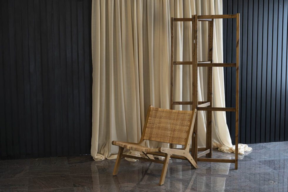 Landscape shot showcasing bohemian photography set. black wood backdrop with neutral and bohemian decor including curtains, room divider, and unique chair.