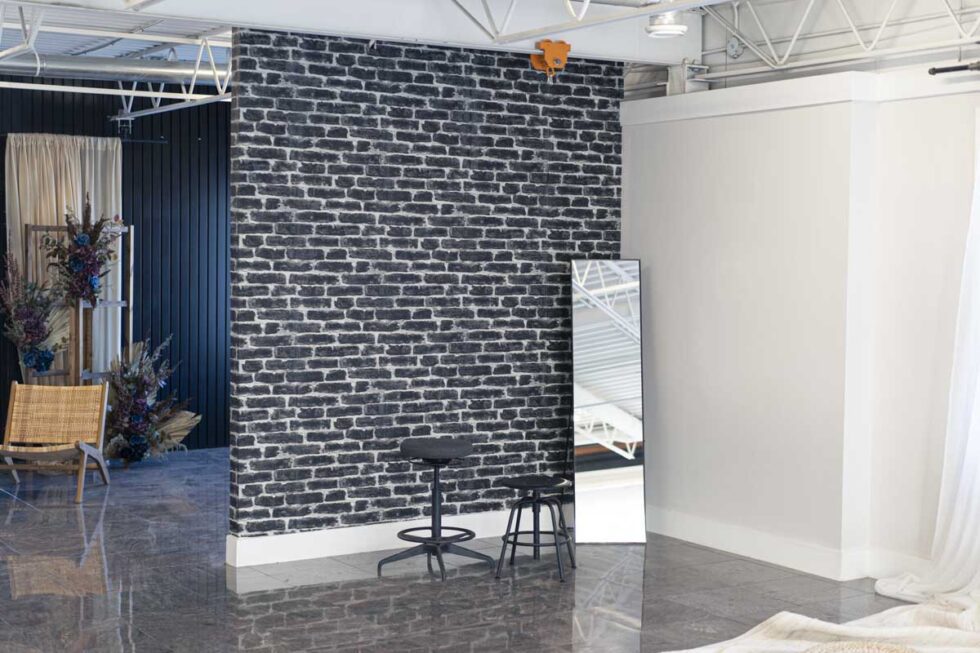 Portrait shot of minimalist industrial photography set. Black and white brick wallpaper with 2 stools and a full length floor mirror.