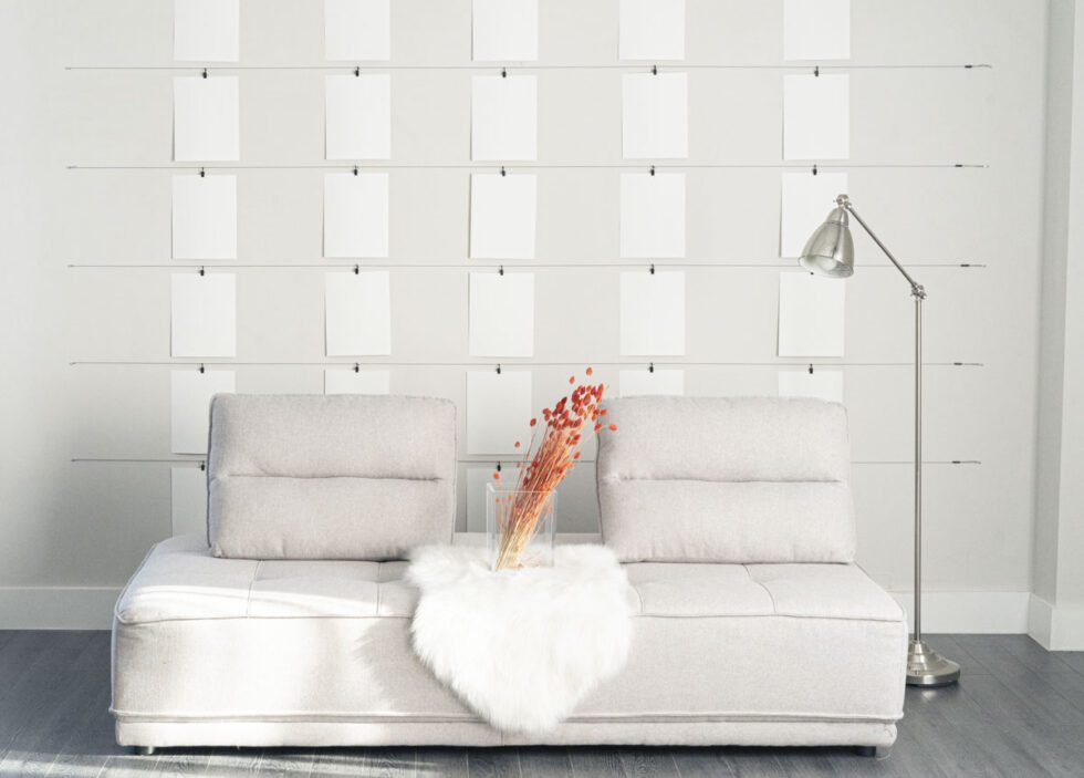 Landscape shot of clean minimalist photography set . Natural fiber light grey couch with small white fur and dried red flowers. natural sunlight spills in from nearby window