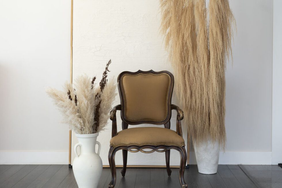Landscape shot of royal photography set. Antique chair centered between potted pampa grasses with large textured artwork behind