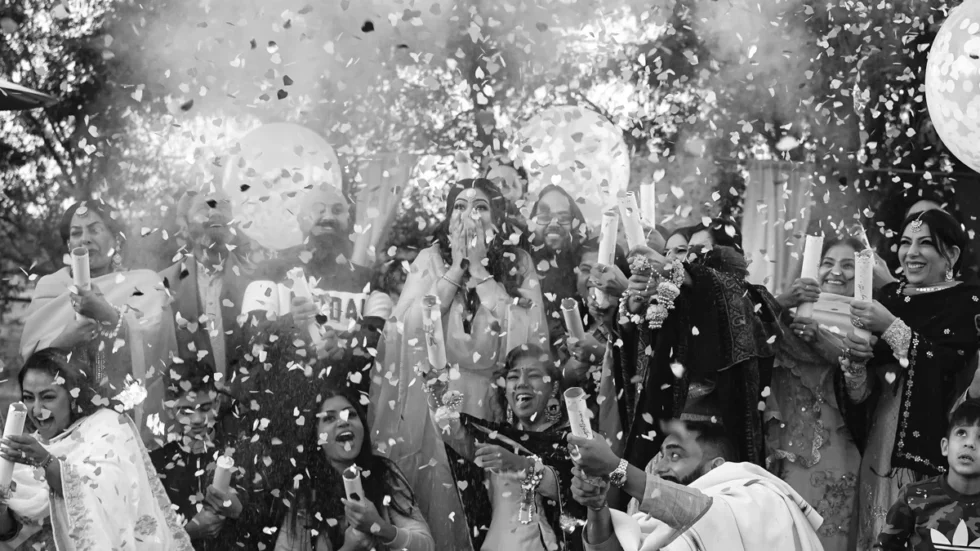 Large family group celebrating a gender reveal with confetti poppers outdoors