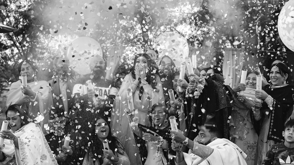 Large family group celebrating a gender reveal with confetti poppers outdoors