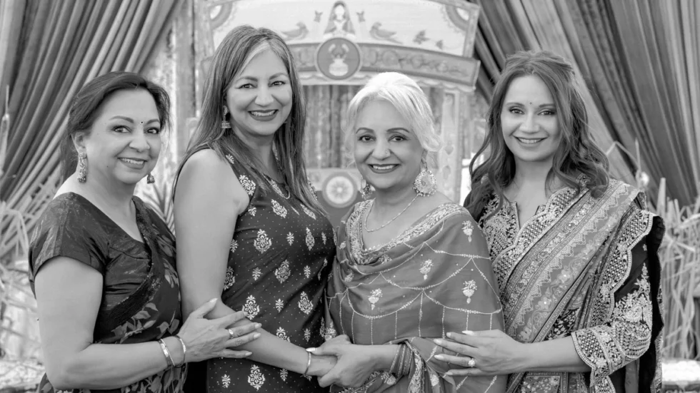 Four women standing together in traditional Indian attire, smiling at the camera