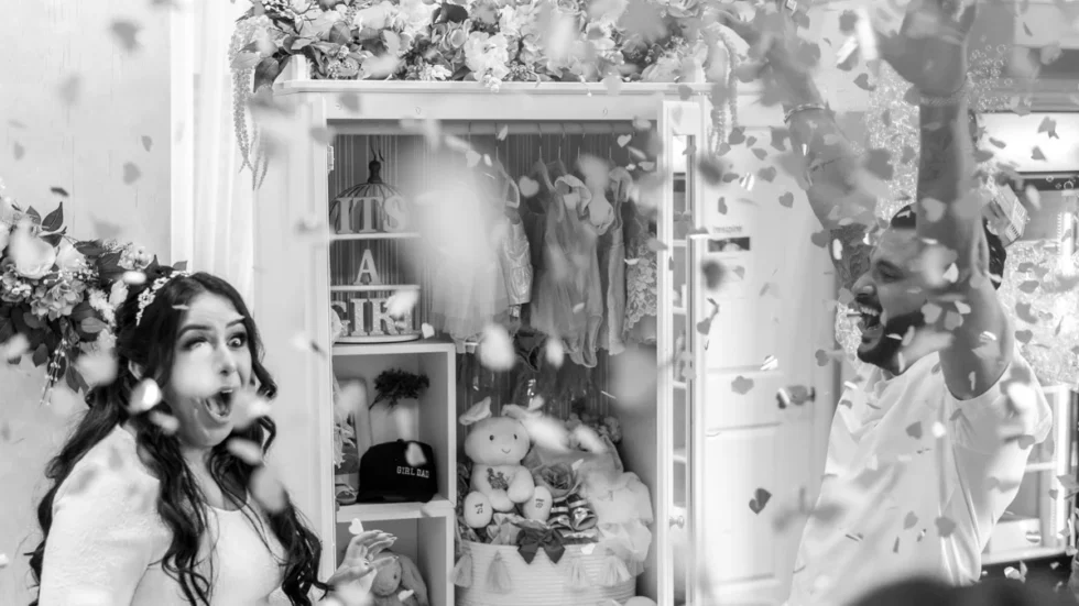 Couple reacting with excitement during a gender reveal celebration with confetti in the air