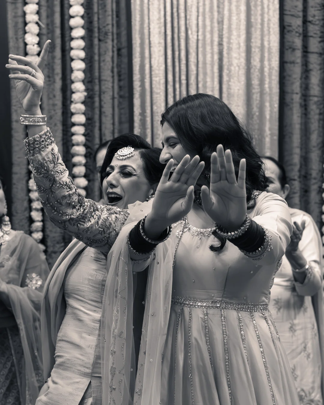 Two women dancing with joyful expressions during a celebration at a Punjabi wedding