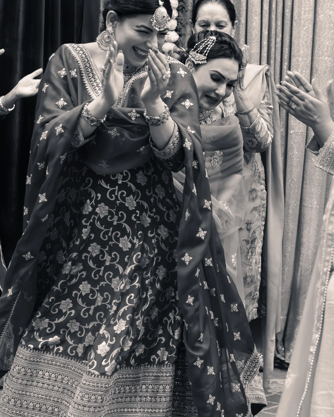 Women laughing and dancing together in traditional outfits during a candid moment at a wedding reception