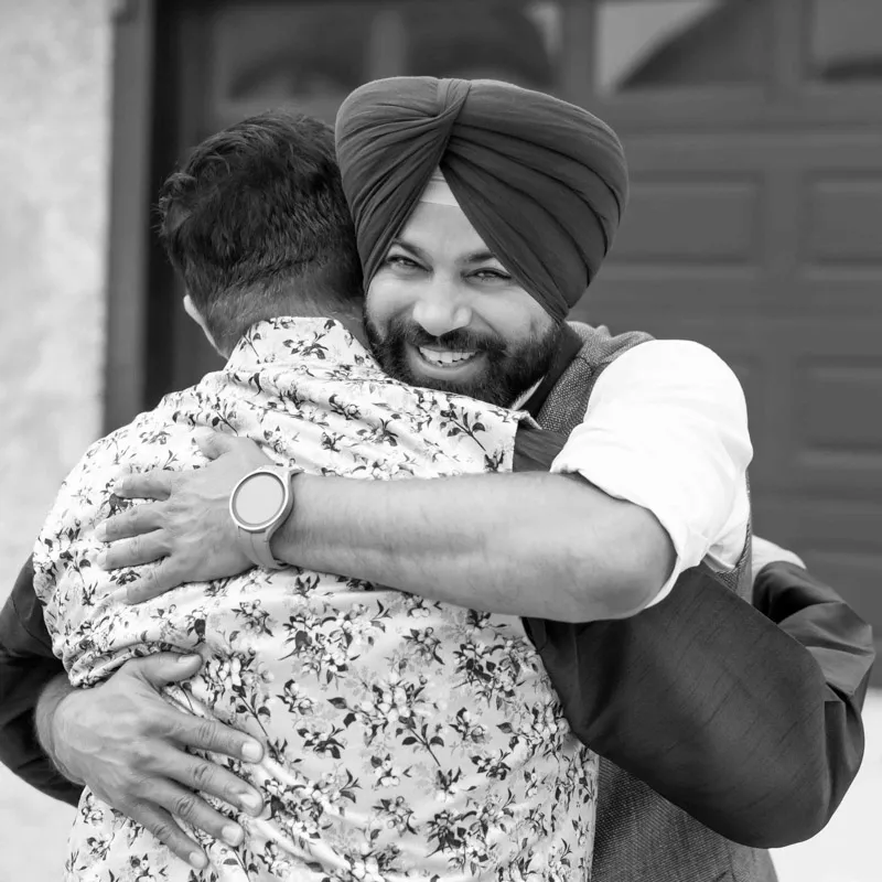 man in a turban smiling while embracing a friend during a joyful greeting at an outdoor event