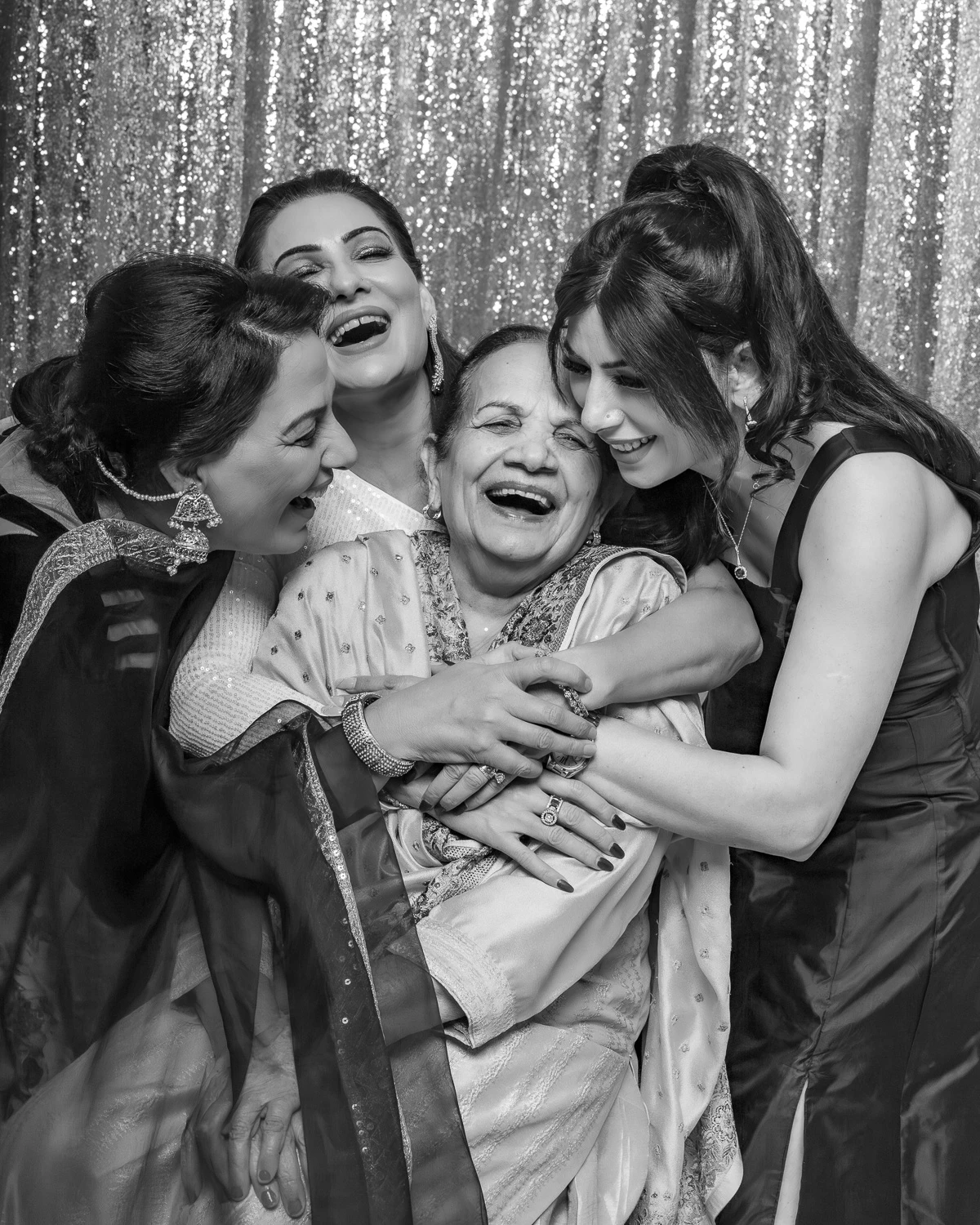 Two women performing a high-energy dance at an Indian celebration, surrounded by smiling family members